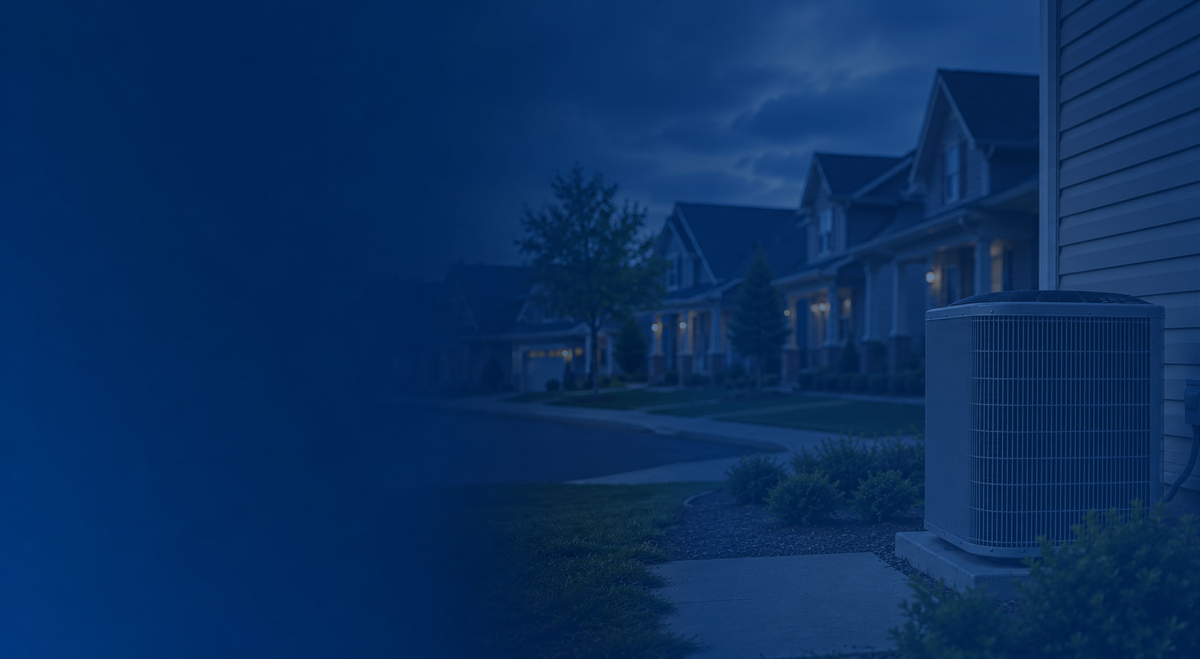 Blue-toned suburban homes at dusk with a lit porch and air conditioner unit