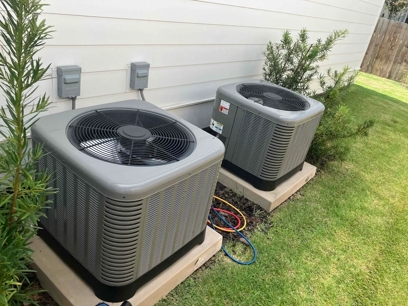 Two outdoor air conditioning units beside a house on a grassy lawn.